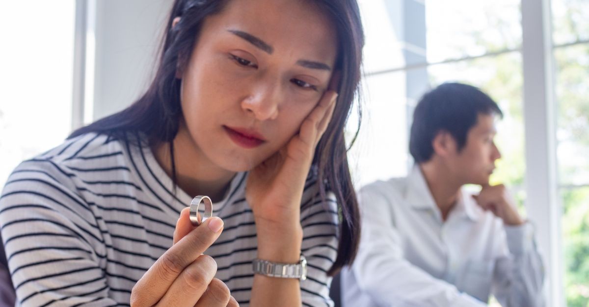 Married couple feuding, the woman looking down at a wedding ring in her hand.